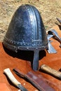 Medieval conical helmet also called norman casque with nosepiece displayed with knives and light battleaxe head displayed on orang