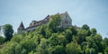 Medieval europe style castle among fresh green forest on top of hill with blue sky background Royalty Free Stock Photo