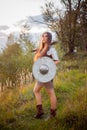 A medieval female warrior dressed in chain mail with a sword and shield in her hands poses against the background of a forest.