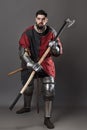 Medieval knight on grey background. Portrait of brutal dirty face warrior with chain mail armour red and black clothes