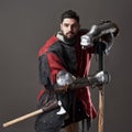 Medieval knight on grey background. Portrait of brutal dirty face warrior with chain mail armour red and black clothes