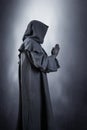 Medieval monk in hooded cloak praying in the dark