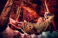 Medieval monk in canvas sackcloth robe with lattern resting on snow in dark forest and red light on winter night. Fantasy or fairy Royalty Free Stock Photo