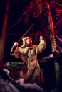 Medieval monk in canvas sackcloth robe with sword and lattern in dark forest and red light of moon on winter night. Fantasy or Royalty Free Stock Photo