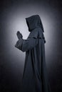 Medieval monk in hooded cloak praying in the dark