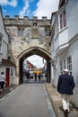 The medieval North Gate, known as the High Street Gate, to the Cathedral Close. Tourists walk along High Street, leading to