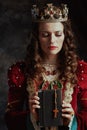 medieval queen in red dress with book, rosary and crown