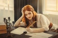 Medieval red-haired woman writer holds pen feather quill in hands, sits at table writes letter on sheet paper. Vintage Royalty Free Stock Photo