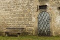 Medieval stone wall castle exterior site background with iron arch door and wooden bench empty yard space rustic environment Royalty Free Stock Photo