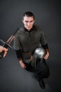 A medieval warrior in chain mail sits on his knee with a helmet in his hands. Knighting