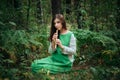 A medieval woman in a green dress plays on a wooden flute sitting in fern bushes. A girl in a gloomy forest plays music on a handm Royalty Free Stock Photo