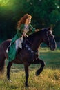 Medieval woman princess in green dress sits astride black steed horse.