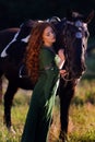 Medieval woman princess in green dress sits astride black steed horse.