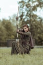 Medieval woman warrior with a bow sits in a clearing and aims from a bow, hunting in a green forest