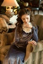 a medieval young lady sits in a cozy antique sofa chair in an old-fashioned interior modestly downcast eyes Royalty Free Stock Photo