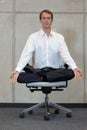 Meditating caucasian businessman in lotus pose on office chair