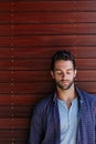 Meditating on life for a moment. a handsome man standing against a wooden wall. Royalty Free Stock Photo