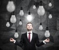 Meditating man is searching new ideas. Lots of light bulbs. Dark contemporary background.