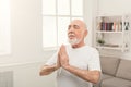 Meditating senior man with praying hands indoors