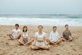 Meditation class outoors. Group of people practicing yoga on the beach, meditating with closed eyes in lotus position Royalty Free Stock Photo