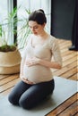 Meditation during pregnancy. Young calm tranquil pregnant woman doing yoga at home, meditating and practicing mindfulness, Royalty Free Stock Photo