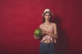 Meditative girl with pink make up, wearing jeans, hat and top, posing at red studio background, holding watermelon, emotionally