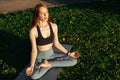 Meditative young woman with closed eyes is meditating sitting in lotus position on yoga mat outside