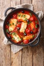 Mediterranean baked Halloumi with tomatoes, peppers, olives in a spicy sauce close-up in a pan. Vertical top view
