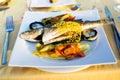 Mediterranean charcoal grilled seabass fish on a white plate with vegetables on the table
