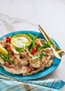 Mediterranean grilled chicken strips served with baked white potatoes and salad of arugula and cherry tomatoes on a blue plate