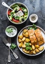 Mediterranean lunch table - baked lemon salmon with potatoes, greek salad, tzadziki sauce on dark background, top view. Flat lay