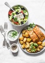 Mediterranean lunch table - baked lemon salmon with potatoes, greek salad, tzadziki sauce on light background, top view. Flat lay