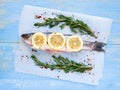 Mediterranean seafood concept. Raw seabass with lemon, spices and rosemary on the parchment paper on light blue wooden