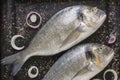 Two fresh raw fishes of sea bream on black baking sheet