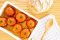 Mediterranean stuffed tomatoes with meat and bread crumbs,  in a white oven dish, aside a kitchen towel, and bread loaf on oak Royalty Free Stock Photo