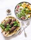 Mediterranean style lunch table. Meat kebab, garlic herb naan, yogurt dressing vegetable salad, roasted potatoes - delicious lunch