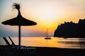 Mediterranean Sunrise off the Mountainous Coast of Mallorca in the Ballearic Islands with Silhouetted Sailboat and Beach Umbrella Royalty Free Stock Photo