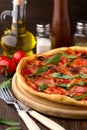 Mediterranean traditional pizza with ham, tomatoes, olives and herbs on wooden table. Royalty Free Stock Photo