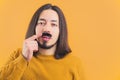 Medium closeup young long-haired man touching fake black moustache yellow background copy space isolated studio shot Royalty Free Stock Photo
