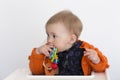 Medium horizontal shot of adorable fair toddler girl sitting in high chair in half profile holding colourful toy to her mouth