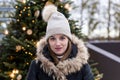 Young girl in fur trimmed black winter coat with lighted Christmas tree in soft focus background