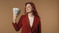 Medium isolated shot of a young woman blowing herself with bills using them like a fan and smiling. Money and cash topic
