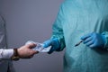 Medium plan portrait of a businessman, a young guy giving dollar bills to the hands of a surgeon in a sterile suit and gloves,