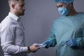 Medium plan portrait of a businessman, a young guy giving dollar bills to the hands of a surgeon in a sterile suit and gloves,