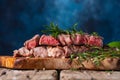 Medium rare grilled beef steak ribeye with rosemary on wooden cutting board on dark blue background. Appetizing image for Royalty Free Stock Photo