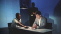 Medium shot of African detective questioning suspect caucasian man in interrogation room. Royalty Free Stock Photo