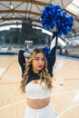 Medium shot. A blond cheerleader in an uniform, with one arm behind her head and the other one stretched up. Sport Royalty Free Stock Photo