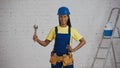 Medium shot of a dark-skinned young female construction worker standing in the room, wearing a tool belt, showing an Royalty Free Stock Photo