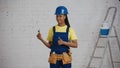 Medium shot of a dark-skinned young female construction worker standing in the room, wearing a tool belt, showing a Royalty Free Stock Photo