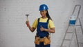 Medium shot of a dark-skinned young female construction worker standing in the room, wearing a tool belt, showing a Royalty Free Stock Photo